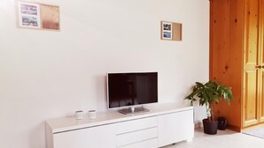 Un saló modern amb un televisor de pantalla plana sobre un moble blanc, un armari de fusta i una planta en test.