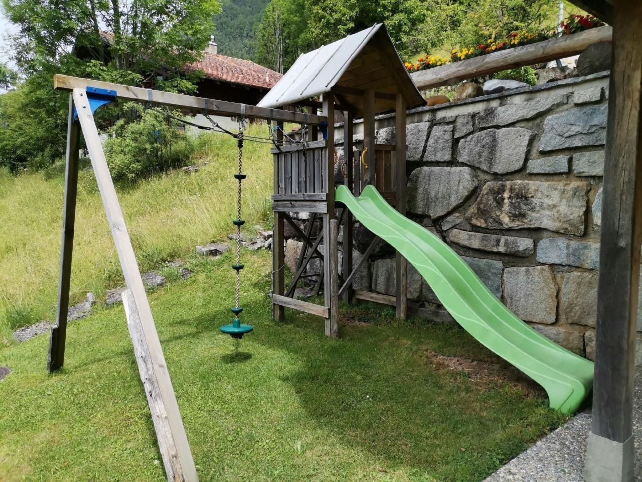 Eine hölzerne Spielkonstruktion mit Rutsche und Schaukeln in einem grünen Garten.