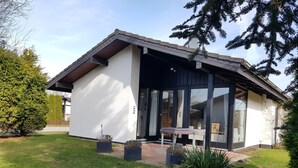 Ein modernes Haus mit einer großen Glasdoor, einer überdachten Terrasse und einem gepflegten Rasen.