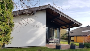 Ein modernes Haus mit überdachter Terrasse, einem kleinen Tisch und Kübelpflanzen.
