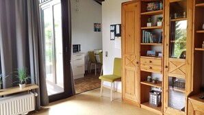 Ein gemütliches Wohnzimmer mit einer Holzregal, einem Essbereich mit Tisch und Stühlen sowie einem großen Fenster mit Vorhängen.