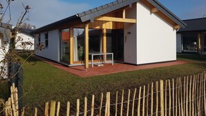 Et moderne hus med træterrasse, store vinduer og et lille bord.