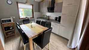 Et moderne køkken med spiseplads, træbjælker i loftet, et ur og et vindue med skodder.