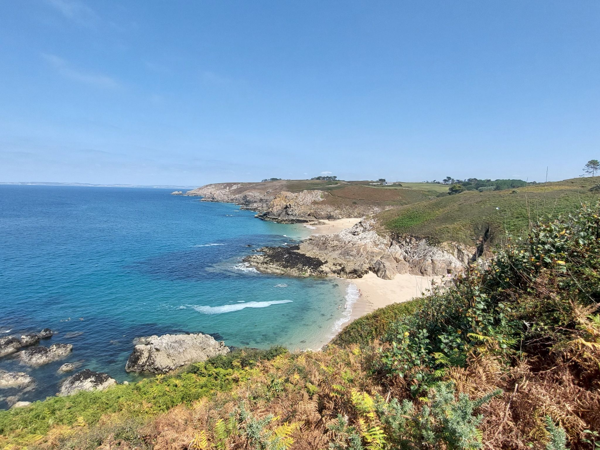 Un paisaje costero con costa rocosa, mar azul cristalino y una colina cubierta de hierba.