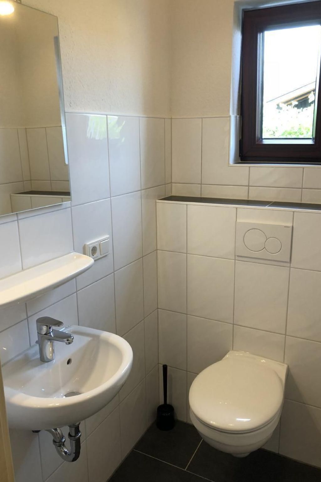 A small bathroom with a white sink, toilet, and a window above the toilet.