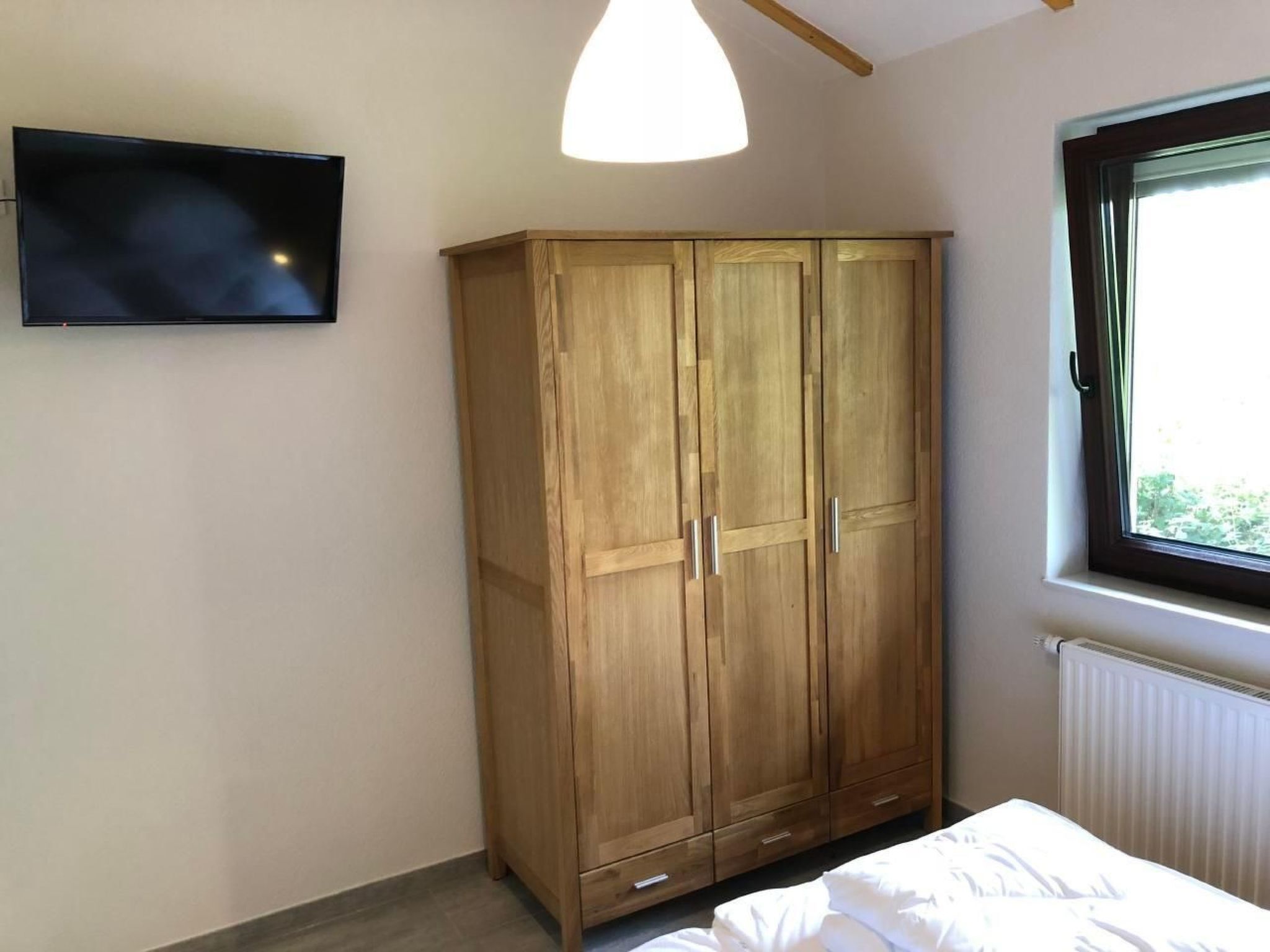 Een slaapkamer met een houten garderobe, een bed, een televisie en een raam met uitzicht.