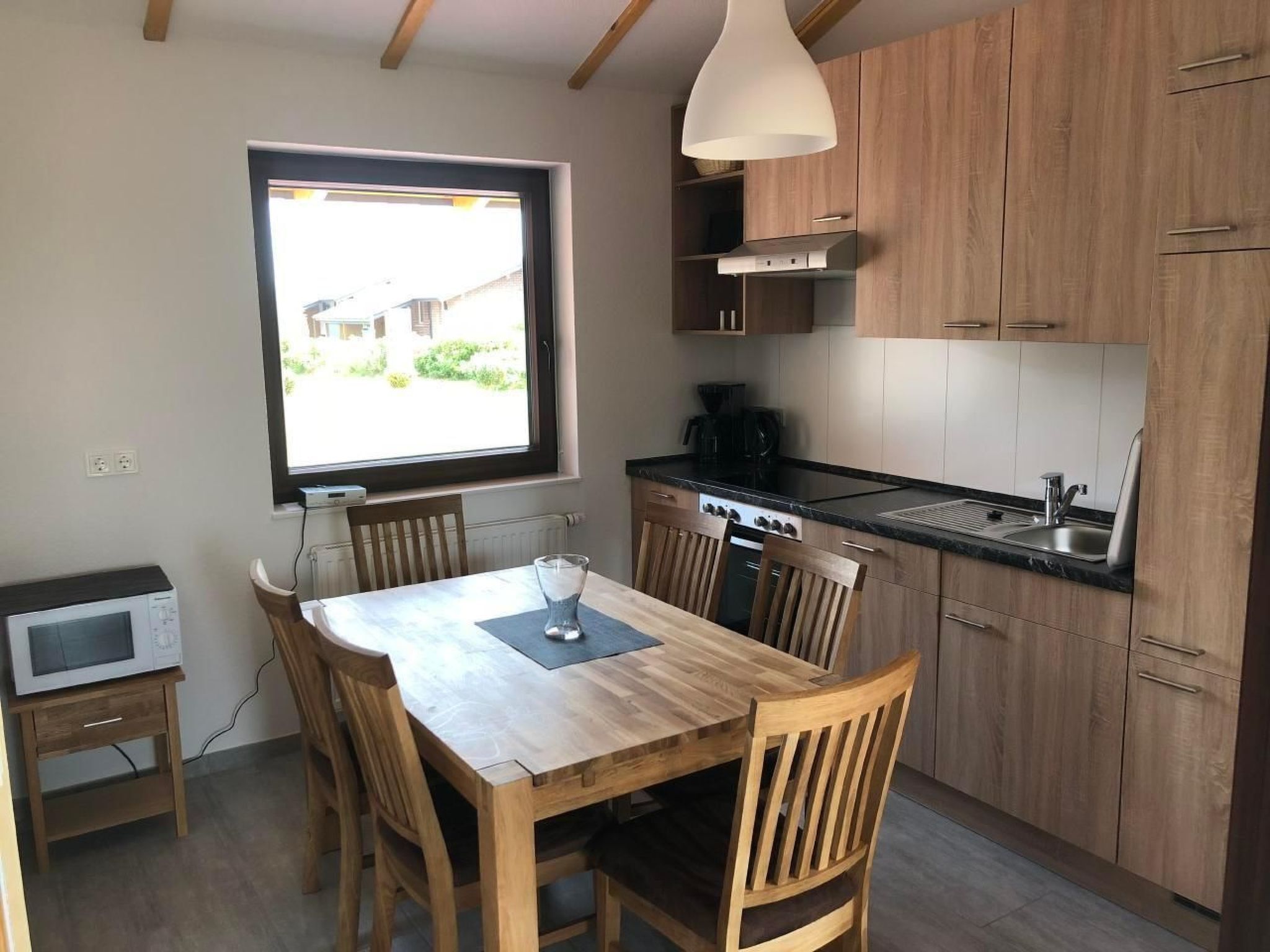 A modern kitchen with wooden cabinets, a dining table with chairs, a built-in oven, and a window with a view of the outside.