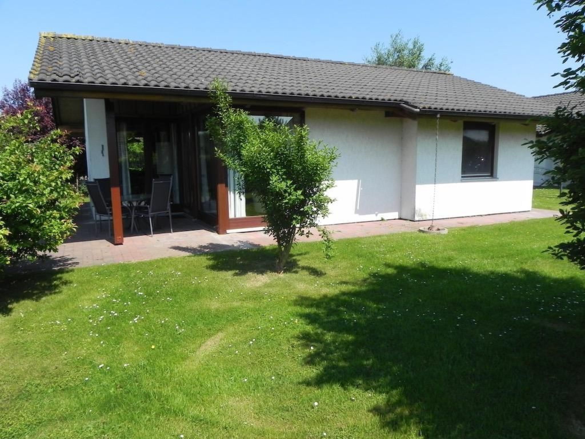 A single-story building with a tiled roof, a covered patio area, and a small lawn.