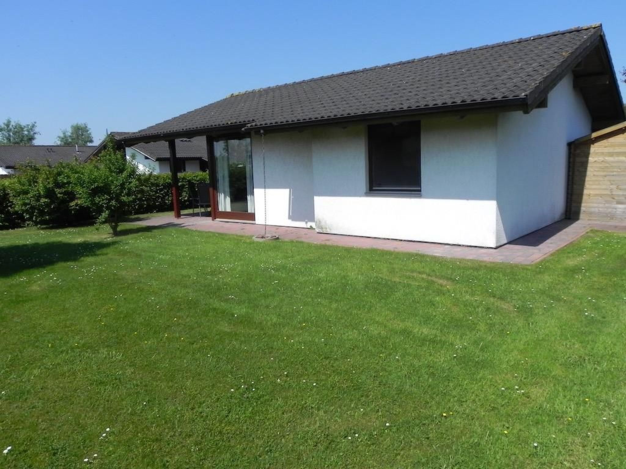 Ein eingeschossiges Haus mit einem geneigten Dach, einer überdachten Veranda und einem gepflegten Rasen.