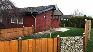 Punainen talo, jossa on satelliittiantenni, puinen aita ja kivimuuri.