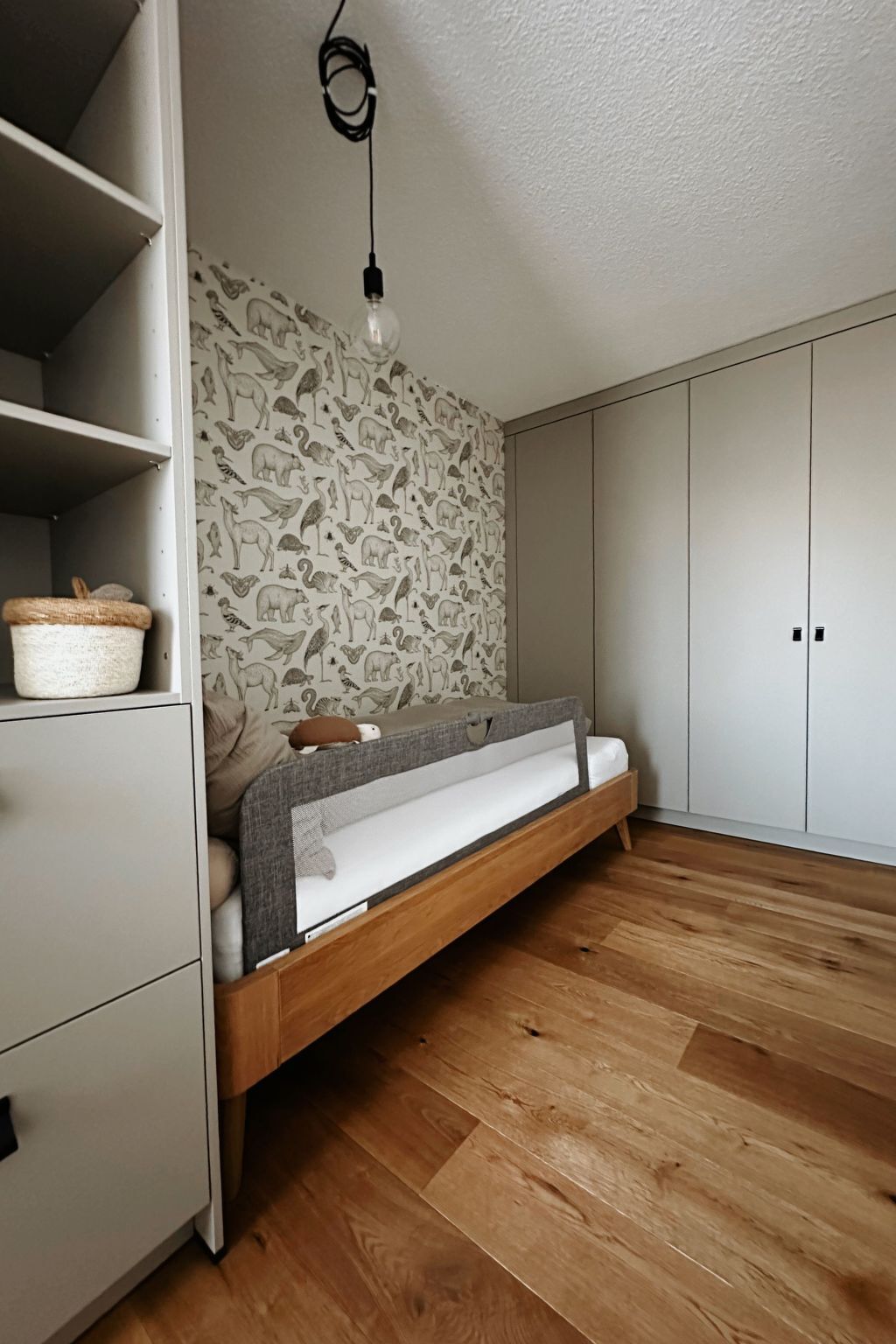 Quarto com cama embutida, parede com estampas de animais, piso de madeira e luminária pendente.