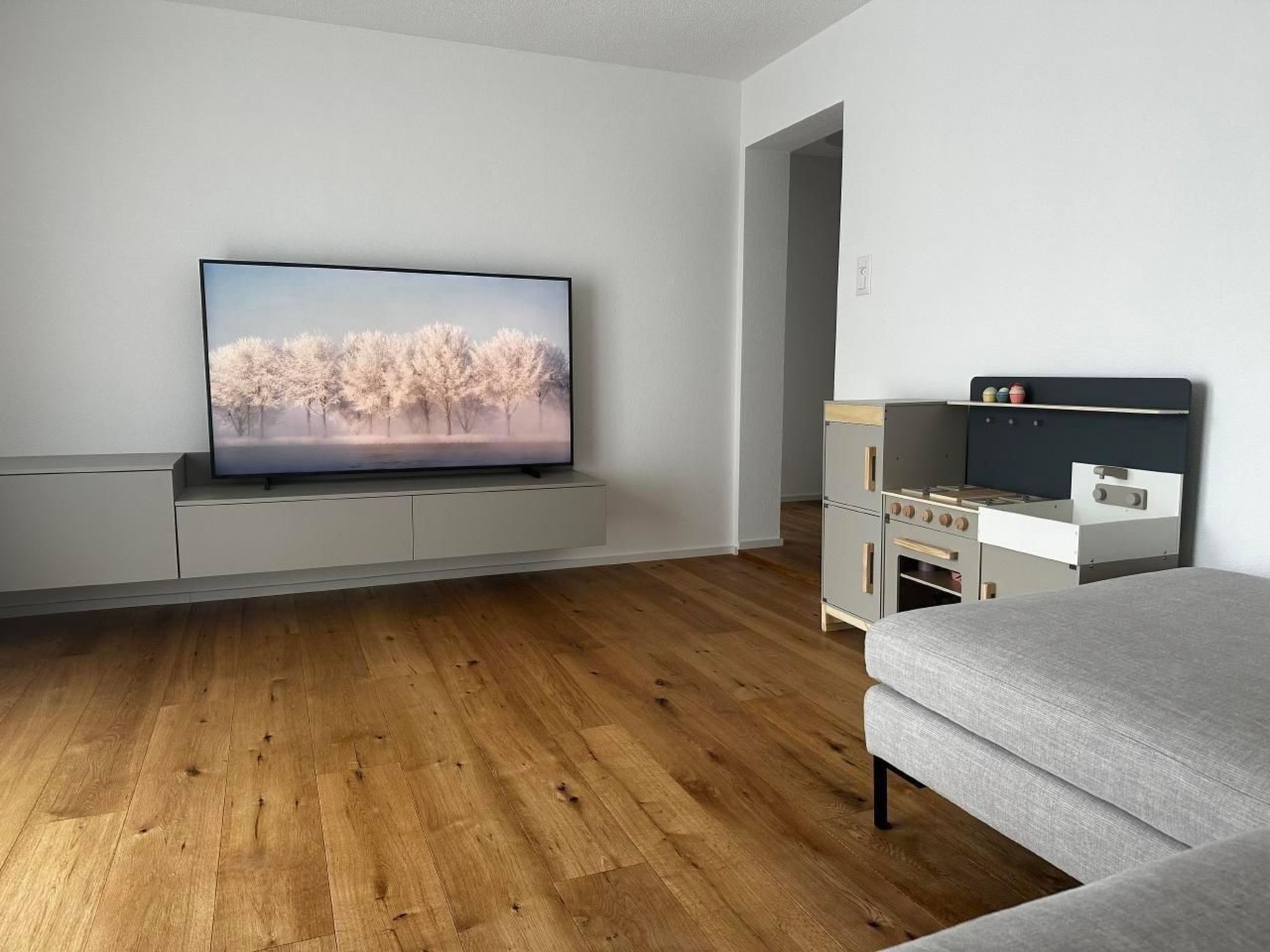 Ein modernes Wohnzimmer mit Flachbildfernseher, Holzboden, einer Couch und einer Küchenzeile.