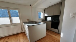 A modern kitchen with a central island, white cabinetry, and a window with blinds. - Sunnuhof Lodge by Interhome (Grächen)