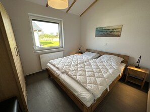 Ein Schlafzimmer mit einem hölzernen Bett, einem Fenster mit Blick auf Grünflächen, einem Gemälde an der Wand und einem Nachttisch mit einer Lampe.
