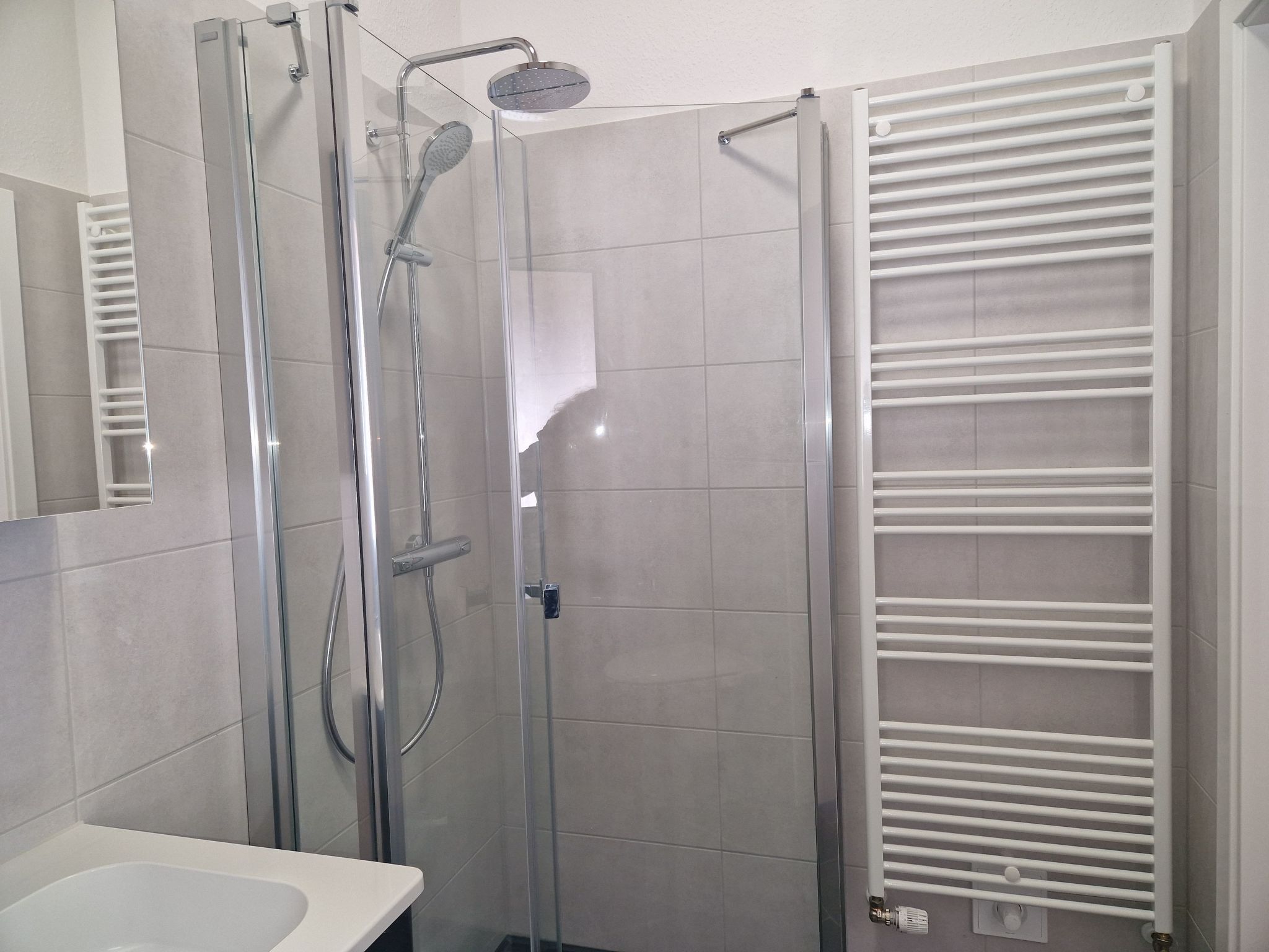 Een moderne badkamer met een glazen douchecabine, een witte wastafel en een handdoekrek.