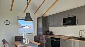 Eine moderne Küche mit grauen Schränken, einer schwarzen Mikrowelle und einer Holz Arbeitsplatte. Ein Esstisch mit vier Stühlen und einer Pendelleuchte darüber.