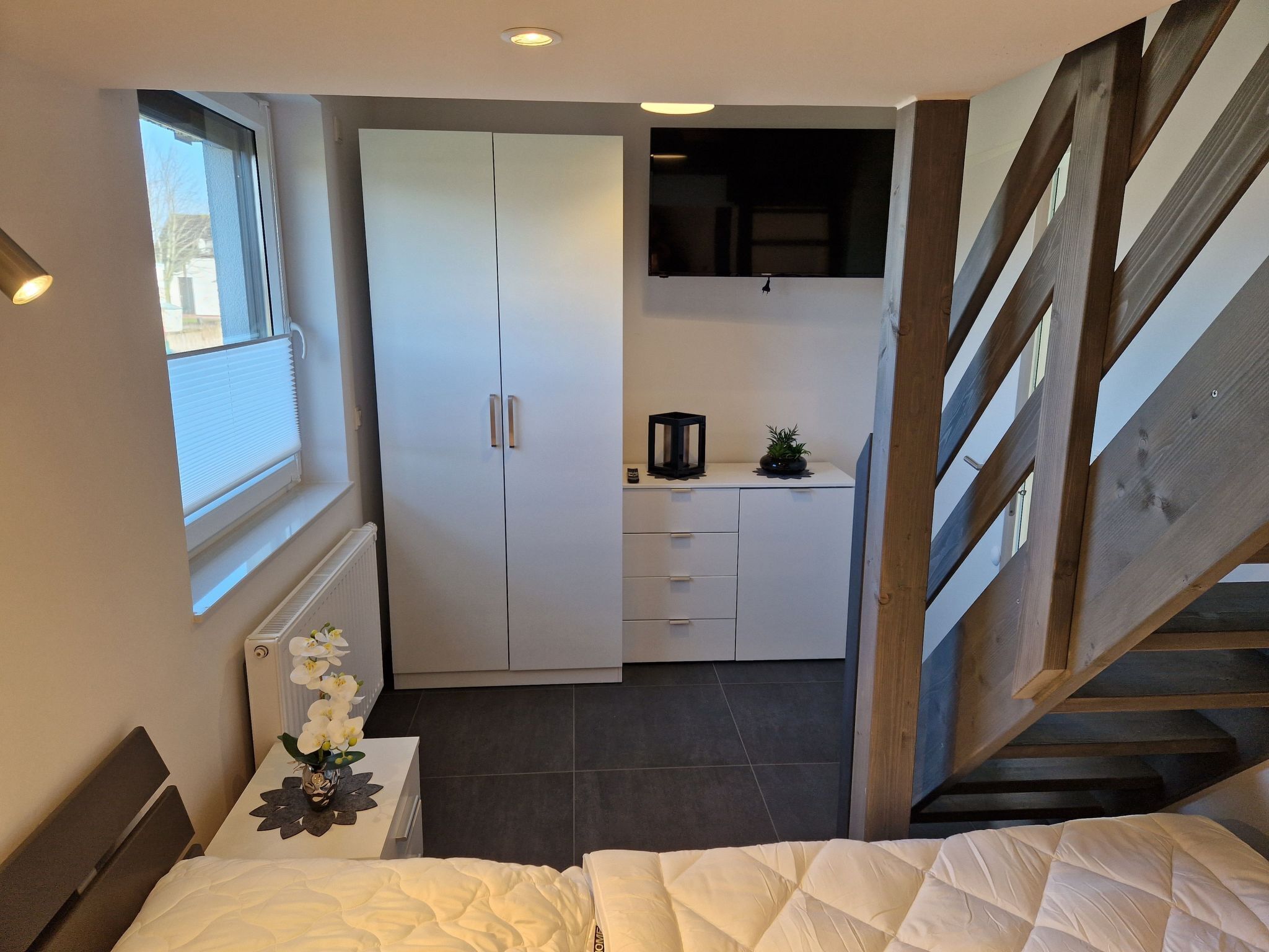 A bedroom with a bed, a wardrobe, a small desk, and a staircase.