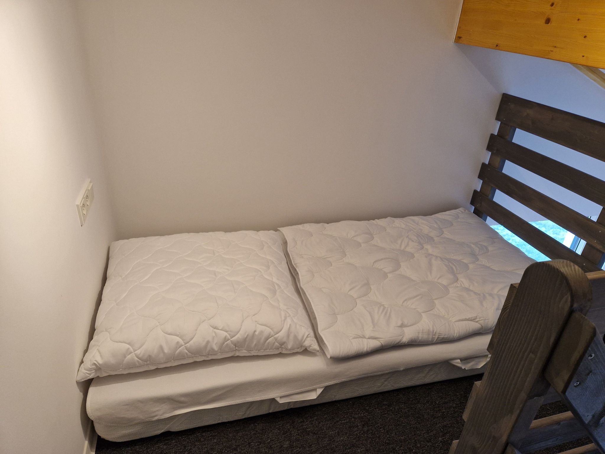 Una piccola camera con un letto singolo, una testiera in legno e una finestra.