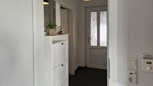 Ein Flur mit einer weißen Kommode, einem Topfpflanzen, einem Glasbehälter und einer Tür mit satinierten Glasscheiben.