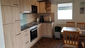 A compact kitchen with wooden cabinets, a built-in oven, a coffee maker, and a window with a view of a tiled roof. - Vacation home  by Interhome (Burhave)