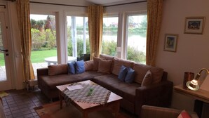 A living room with a brown sofa, a wooden coffee table, and a view of a garden through large windows. - Vacation home  by Interhome (Burhave)