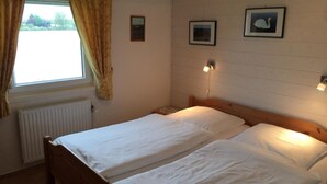 A room with two single beds, a window with curtains, a radiator, and two framed pictures on the wall. - Vacation home  by Interhome (Burhave)