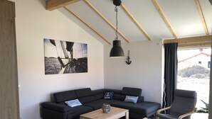A modern living room with a black sofa, a wooden coffee table, and a grey armchair. There is a painting of a sailboat on the wall and a hanging lamp. - N8 Eingezäuntes Ferienhaus in Eckwarderhörne by Interhome (Burhave)