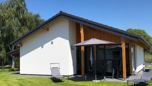 A modern house with a white exterior, wooden beams, and a covered patio area with two lounge chairs and a table. - N8 Eingezäuntes Ferienhaus in Eckwarderhörne by Interhome (Burhave)
