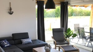 A modern living room with a sectional sofa, a wooden coffee table, and a glass dining table with chairs. - N8 Eingezäuntes Ferienhaus in Eckwarderhörne by Interhome (Burhave)
