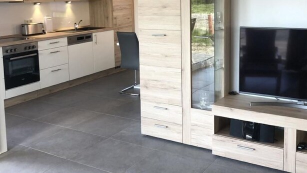 A modern kitchen with wooden cabinets, a built-in oven, and a dining area with a TV. - N8 Eingezäuntes Ferienhaus in Eckwarderhörne by Interhome (Burhave)