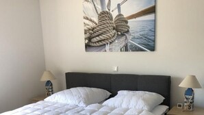 A modern bedroom with a large bed, a dark headboard, a wall-mounted artwork of ropes, and bedside tables with lamps. - N8 Eingezäuntes Ferienhaus in Eckwarderhörne by Interhome (Burhave)
