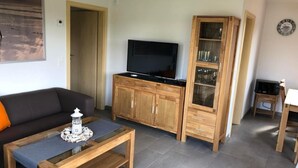 Una sala de estar con sofá, mesa de centro, televisor, armarios de madera y un comedor con mesa y sillas.