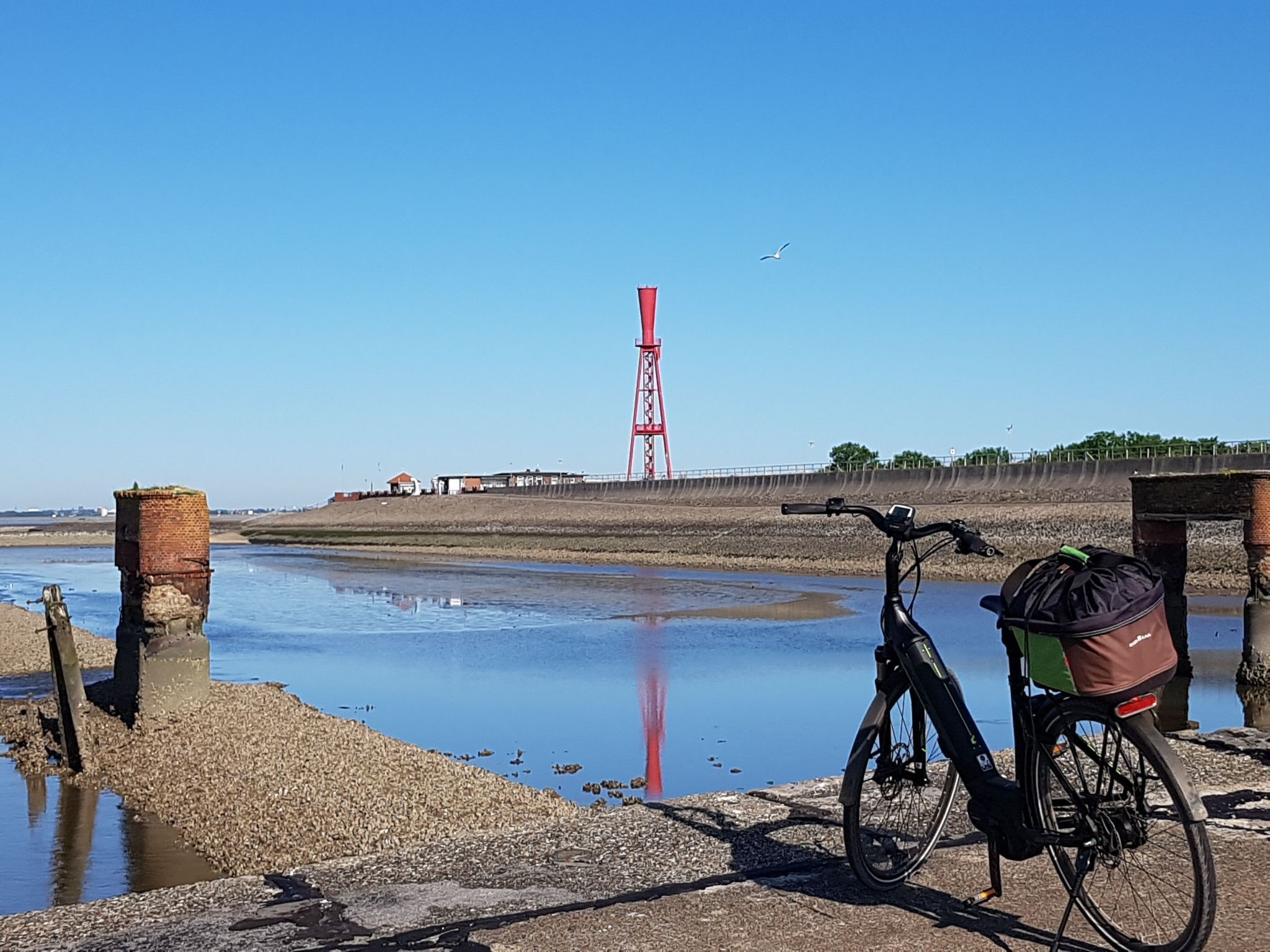 A bicycle parked near a waterfront with a red tower in the background.