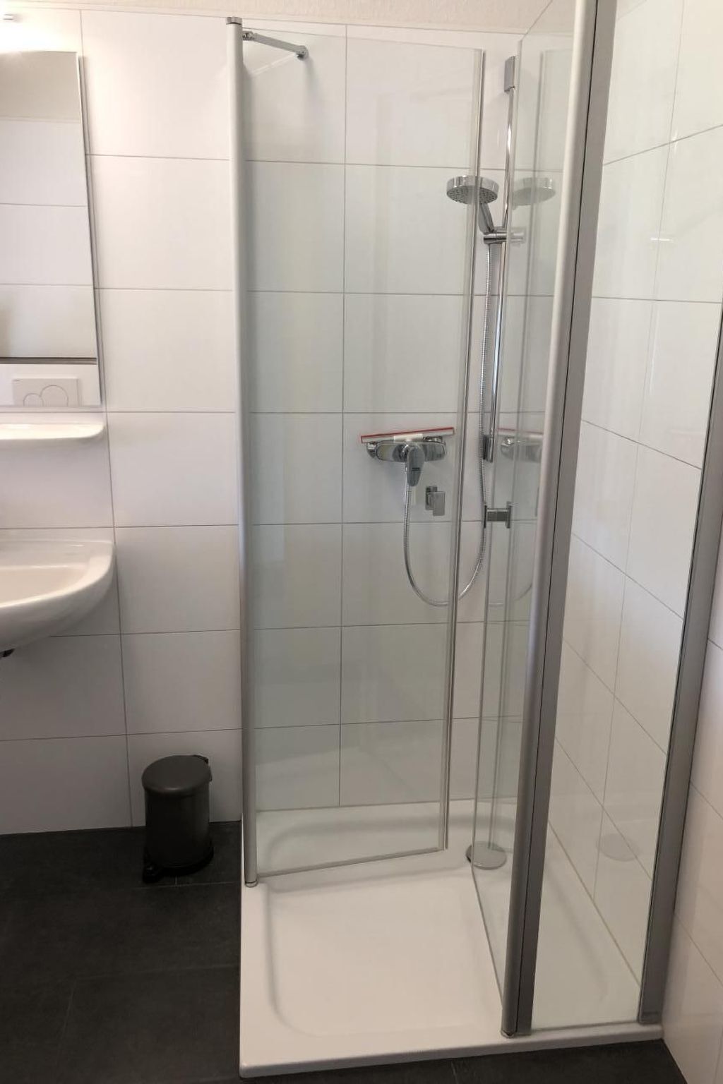 A glass-enclosed shower stall with a handheld showerhead and a wall-mounted faucet.