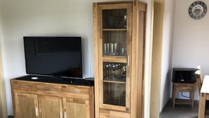 Una sala de estar con un mueble de madera, un televisor de pantalla plana y un aparador con vidrio que exhibe cristalería.