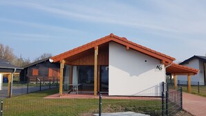 Una casa de una sola planta con techo rojo, un porche cubierto y un pequeño patio.