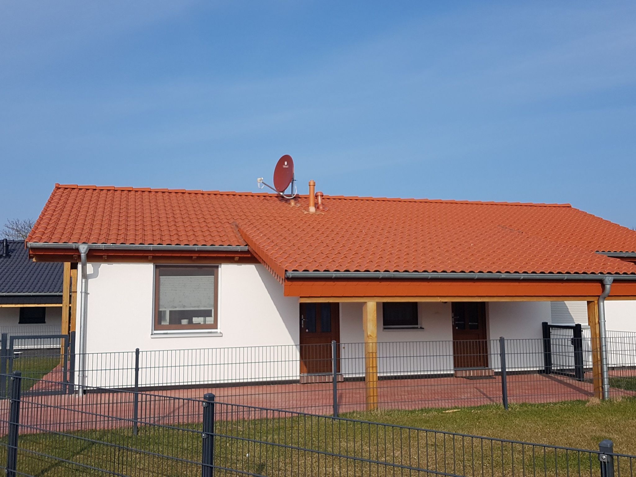 Een laag gebouw met een rode dakbedekking, witte muren en een klein portaal.