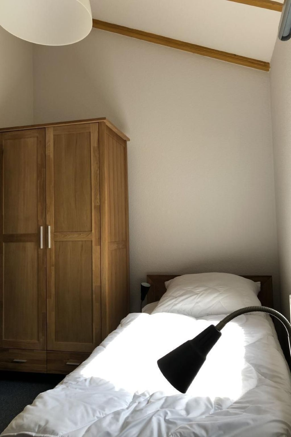 Un dormitorio con cama, armario de madera y lámpara en el techo.