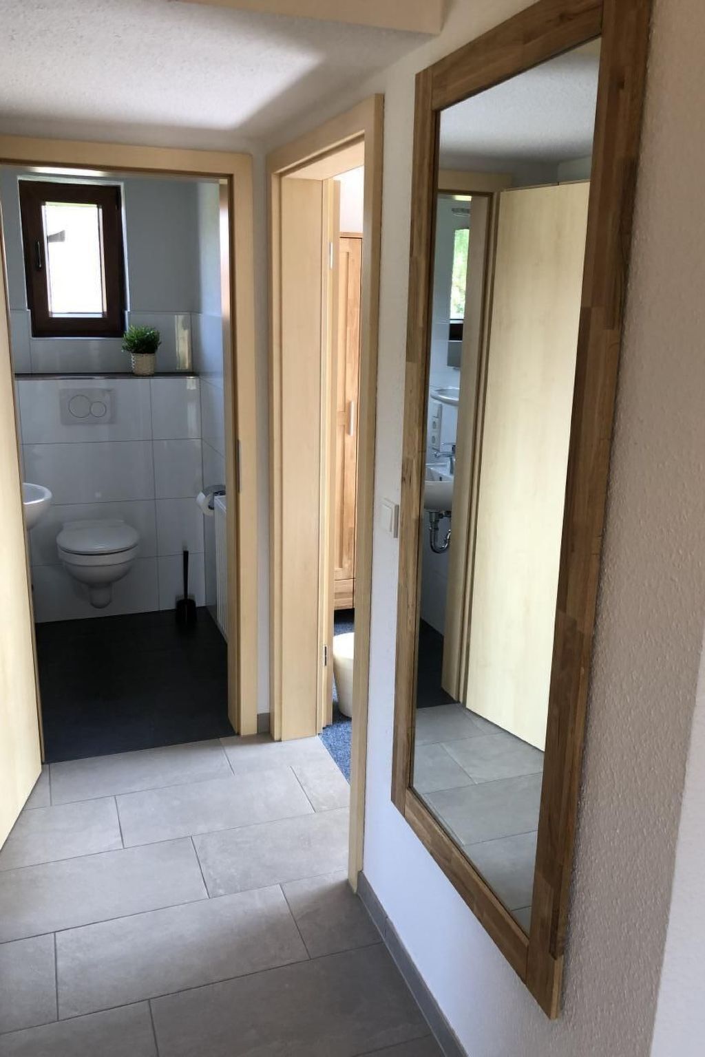 Un couloir étroit mène à une salle de bain équipée de toilettes, d’un lavabo et d’une petite fenêtre.