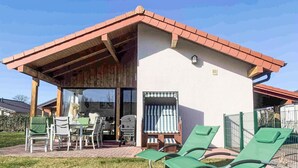 Ein kleines Gebäude mit einem Ziegeldach, einer überdachten Terrasse mit Gartenmöbeln und einem Fenster mit Jalousien.
