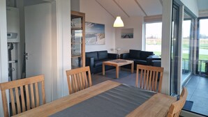 A dining area with a wooden table and chairs, a sofa, and a glass door leading to a balcony. - Vacation home G30 by Interhome (Burhave)