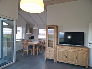 A modern kitchen with a dining area, a TV, and a cabinet with glass doors. - Vacation home G30 by Interhome (Burhave)