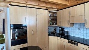 A modern kitchen with wooden cabinets, a black countertop, and a tiled backsplash. - Chalet Luisa by Interhome (Bellwald)
