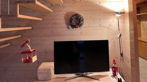 A modern living room with a flat-screen TV on a white entertainment unit, a wooden staircase, and a wall-mounted wreath. - Chalet Luisa by Interhome (Bellwald)
