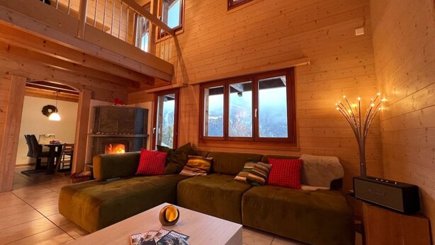 A cozy wooden cabin interior with a living area featuring a sofa set, a fireplace, and a dining area with a table and chairs. - Chalet Luisa by Interhome (Bellwald)