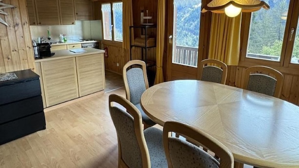L’intérieur d’un chalet en bois comprend une table à manger, des chaises, un coin cuisine et de grandes fenêtres.