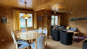 Un intérieur en bois avec une table de salle à manger ronde, des chaises rembourrées bleues, un canapé et un téléviseur.