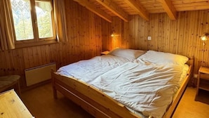 Une chambre dans une cabane en bois, avec un lit simple, une fenêtre avec des rideaux et une petite table.