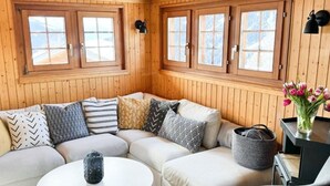 Un interior de cabaña acogedor, con un sofá modular, una mesa de centro redonda y una mesita auxiliar con un jarrón de flores.