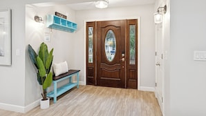 A hallway with a wooden door, a bench, a potted plant, a light fixture, and a wall-mounted shelf. - 7 Strath Court @ Palmetto Dunes | Private Pool | Pet Friendly | Cozy Loft | Spacious Kitchen (Hilton Head Island)
